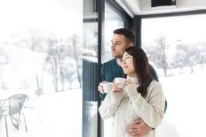 Couple observant le paysage enneigé derrière une baie vitrée coulissante triple vitrage